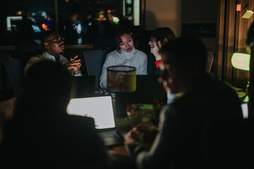 A group of business professionals collaborates during a late-night office meeting. They discuss strategies, engaging in a focused and productive work session, illuminated by the glow of laptop screens