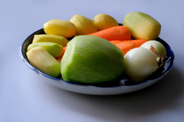 peeled vegetables: potatoes, carrots, radish, and onions lying in a blue bowl.