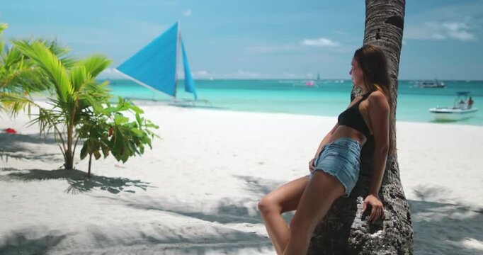 Tourist is enjoying a sunny day at white beach, philippines, relaxing under a palm tree with a traditional paraw sailboat in the background