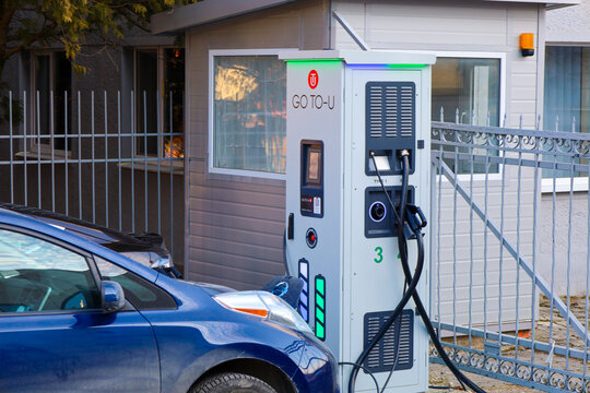 Truskavets, Ukraine, - February 23, 2025: The station is white with the inscription "GO TO-U" and other markings. A blue electric car is parked next to it, connected to the station with a cable.