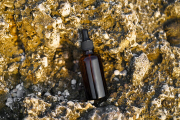 Close-up of brown mock-up serum jar with dispenser on limestone rock near the sea. Natural cosmetics for skin care and renewal, wrinkle reduction, hydration and radiance.