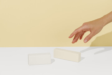 Female hand reaching for yellow mockup boxes on yellow background. Beauty, health and confectionery products, packaging for your design, branding and advertising