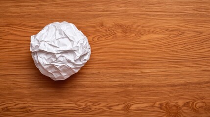 Crumpled paper ball resting on a wooden surface captures the essence of creativity and discarded ideas
