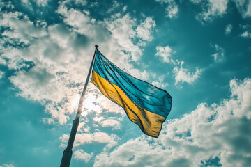 A majestic and inspiring image of the Ukrainian flag waving proudly in the wind against a bright blue sky with scattered white clouds.  