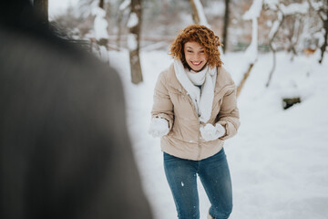 A cheerful young woman in a snowy park holding a snowball, enjoying a playful winter moment as part...
