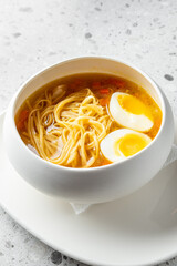 A delicious bowl of noodles soup featuring vibrant broth, tender noodles, and two halved soft-boiled eggs, presented in a minimalist white bowl on a textured surface.