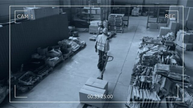 Wide high-angle CCTV security camera shot of male employees in hardhats and visibility vests working in spacious warehouse, transporting boxes on hydraulic trolley checking pallets