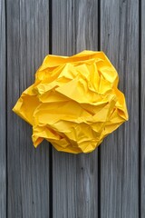 Bright yellow crumpled paper ball placed on a rustic wooden surface for artistic texture and color contrast