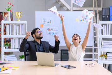 Young Asian businesswoman and businesswoman sitting work at office desk with laptop celebrating...