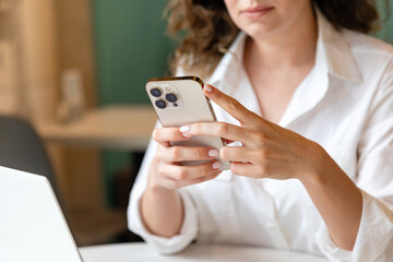 Young woman use cellphone, sit at table, share text messages in social media, enjoy new vlog, watch...