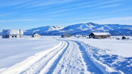 Snow-covered landscape with distant mountains, rural houses, and clear blue sky in winter