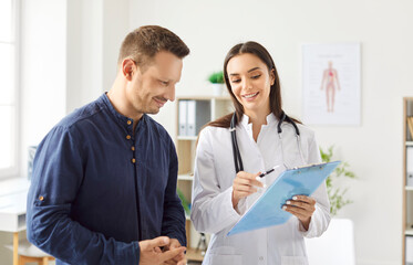 Portrait of a young man patient in medical office listening to a friendly female doctor holding...