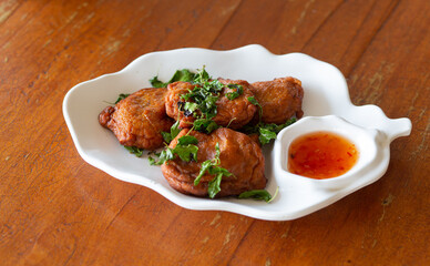 Fish cakes with vegetables and dipping sauce on a white plate on a wooden background.