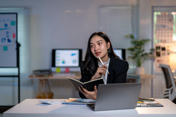 Fototapeta premium A woman is sitting at a desk with a laptop and a notebook