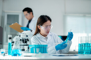 Female scientist in white lab coat and protective gloves analyzing blue liquid sample, research...
