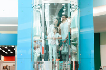 Father, mother and daughter are going down in elevator in shopping mall.