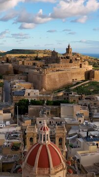 Aerial Vertical view of Historic fort, Citadel Ruins on cliff overlooking valley at sunset with lush greenery in the background. island Gozo. Malta