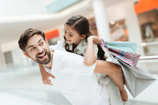 Father carries daughter on back in shopping mall. Girl and man are excited.