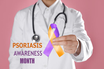 Psoriasis Awareness Month. Doctor holding orange-orchid awareness ribbon on pink background, closeup