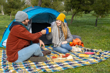 Happy couple camping and toasting with hot drinks in front of tent