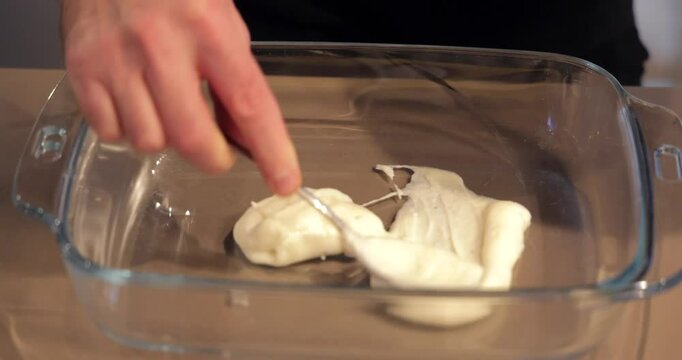 Spoon spreads the first layer of creamy bechamel sauce in a glass baking dish, preparing the base for Italian lasagna before layering other ingredients