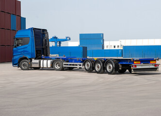 A blue semi truck is parked in front of a large stack of containers