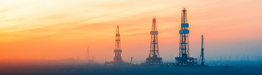 Obraz premium Oil rigs silhouetted against a colorful sunset sky in a serene industrial landscape.