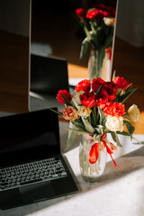 Spring workspace with laptop and vase of tulips bathed in sunlight for online projects