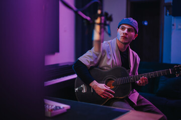 A focused musician plays guitar, creating music in a vibrant recording studio setting. The dim...