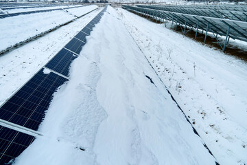 Aerial view of sustainable electrical power plant with solar photovoltaic panels covered with snow in winter for producing clean energy. Concept of low effectivity of renewable electricity in north