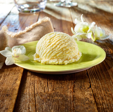 Eiskugel Vanille mit hellen Blueten Glaskanne und Glaesern auf rustikalem dunklem Holzfond mt hellgruenem Fond, Eiscreme, Vanilleeis, Eiskugel,