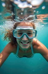 Naklejka premium Smiling girl with diving goggles underwater in bubbly blue water. Curly hair child swimming happily in clear pool water, sunny summer vacation, holidays activity.