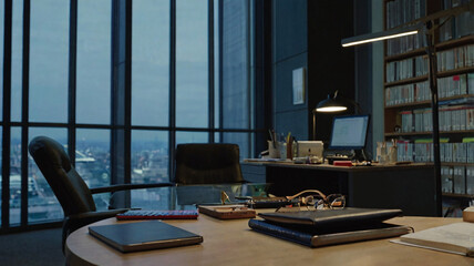 Obraz premium An office space at dusk with a large window offering a city view, a desk holding office items like notebooks and glasses, a computer setup, and a bookshelf filled with books.