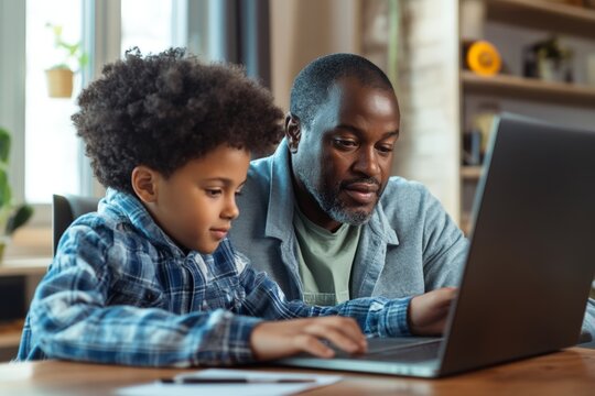 African male adult teaching young child on laptop at home