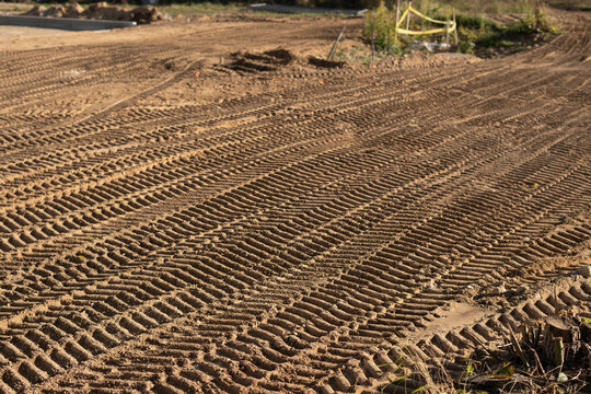 photo Close-up view of intricately patterned tire tracks imprinted on the sandy terrain at a construction site, revealing the heavy machinery's movement and landscaping work