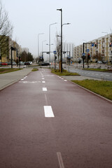 Urban street with cycle path and pedestrian walkway surrounded by residential buildings, featuring traffic lights and street signs under a cloudy sky