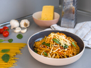 Balanesi pasta topped with tomato sauce, fresh basil, and grated cheese, served in a modern bowl with kitchen ingredients and utensils creating an inviting culinary scene