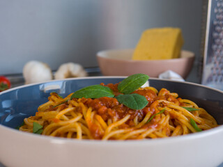Balanesi pasta with basil leaves and tomato sauce is served in a bowl, ready to be eaten, with ingredients and kitchen utensils in the background