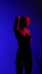 Blonde with a beautiful figure in a black patent leather bodysuit poses in a studio. Studio lighting, low exposure, monochrome red light