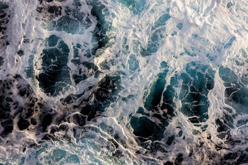 Ocean water surface texture. Aerial view of captivating water with foam. Can be used in covers, packaging, posters, textures, presentations, art, and design projects. Artistic nature background image.