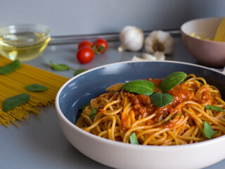 Homemade balanesi pasta drizzled with bright red tomato sauce, garnished with fresh basil leaves, resting in sleek ceramic bowl against softly blurred kitchen backdrop
