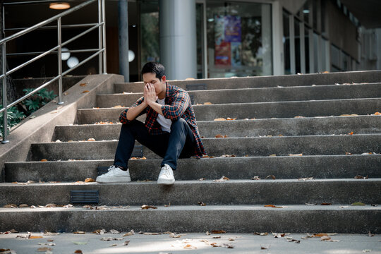 Exhausted college student sitting on campus stairs, hands covering face, experiencing overwhelming academic stress and emotional distress