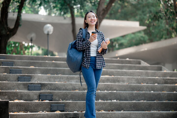 Obraz premium Young asian student climbing university stairs, carrying books, coffee, backpack, wearing casual outfit