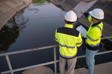 A engineering doing his checking routine. He is wearing hard hat and engineer uniform.Standing by the rail by the dam.Monitor water levels from the heavy rain that has been falling for several days.