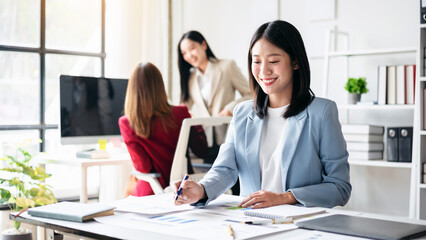 A woman is sitting at a desk with a pen and paper, smiling