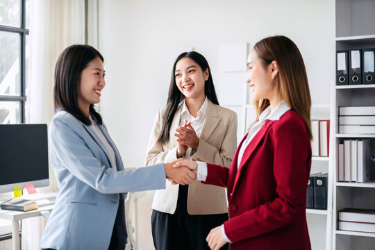 Three women in business attire shake hands and smile at each other