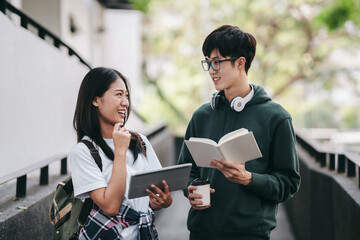 Two young people are walking down a sidewalk, one of them holding a book