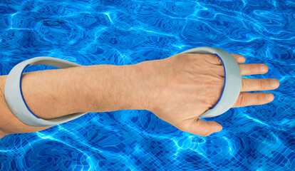 A Swimming Forearm Fulcrum worn on the arm to improve stroke technique against a blue swimming pool...