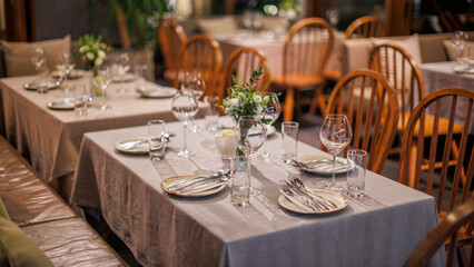 An elegantly set restaurant table with fine dining arrangements, including wine glasses, silverware, and a floral centerpiece, creating a warm and inviting ambiance.