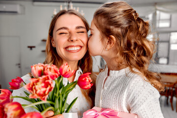 Happy Mother’s Day! A little girl kisses her mom while congratulating her with a bouquet of...